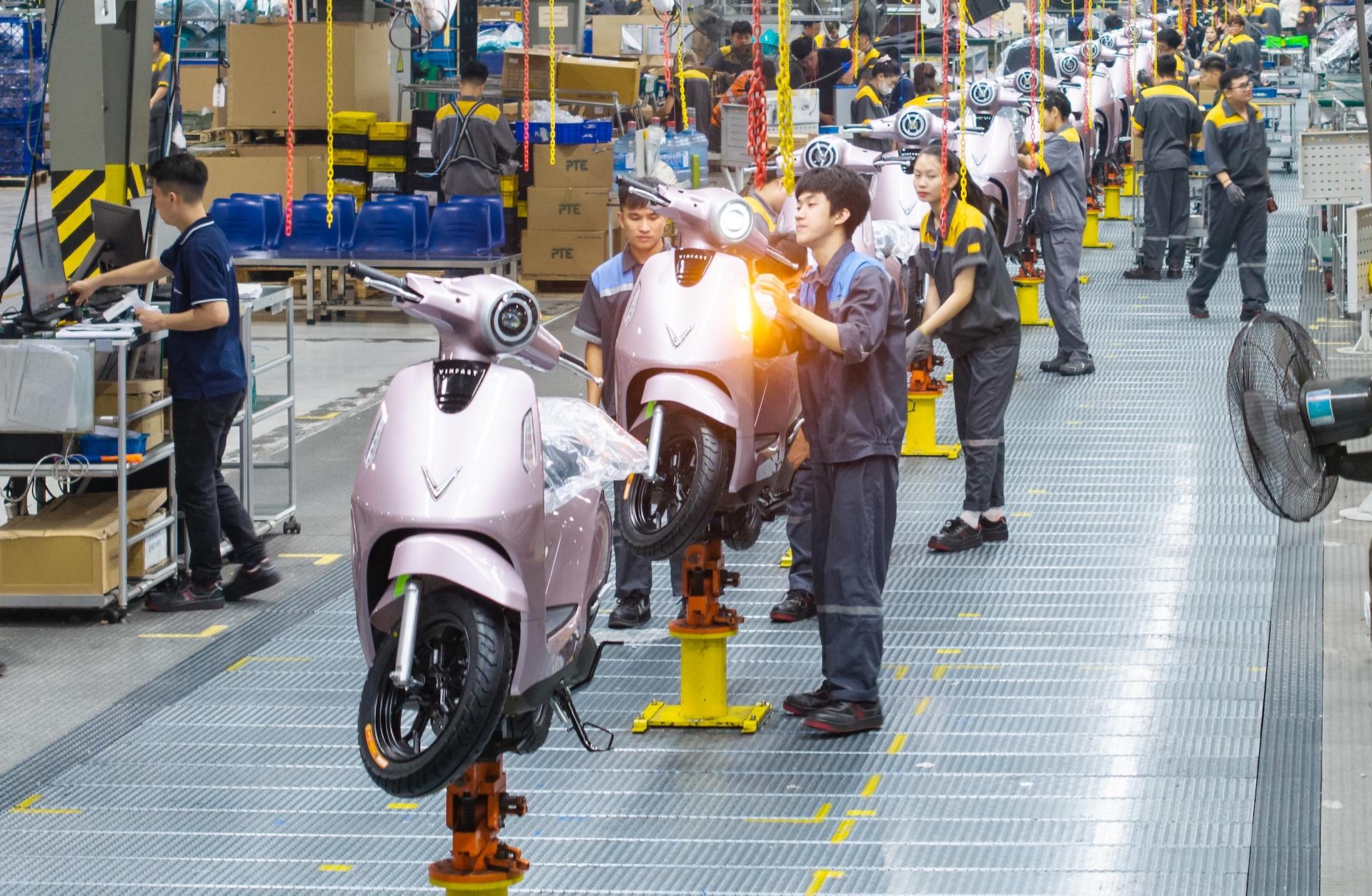 Công nhân lắp ráp các xe máy điện màu hồng nhạt trên dây chuyền sản xuất.