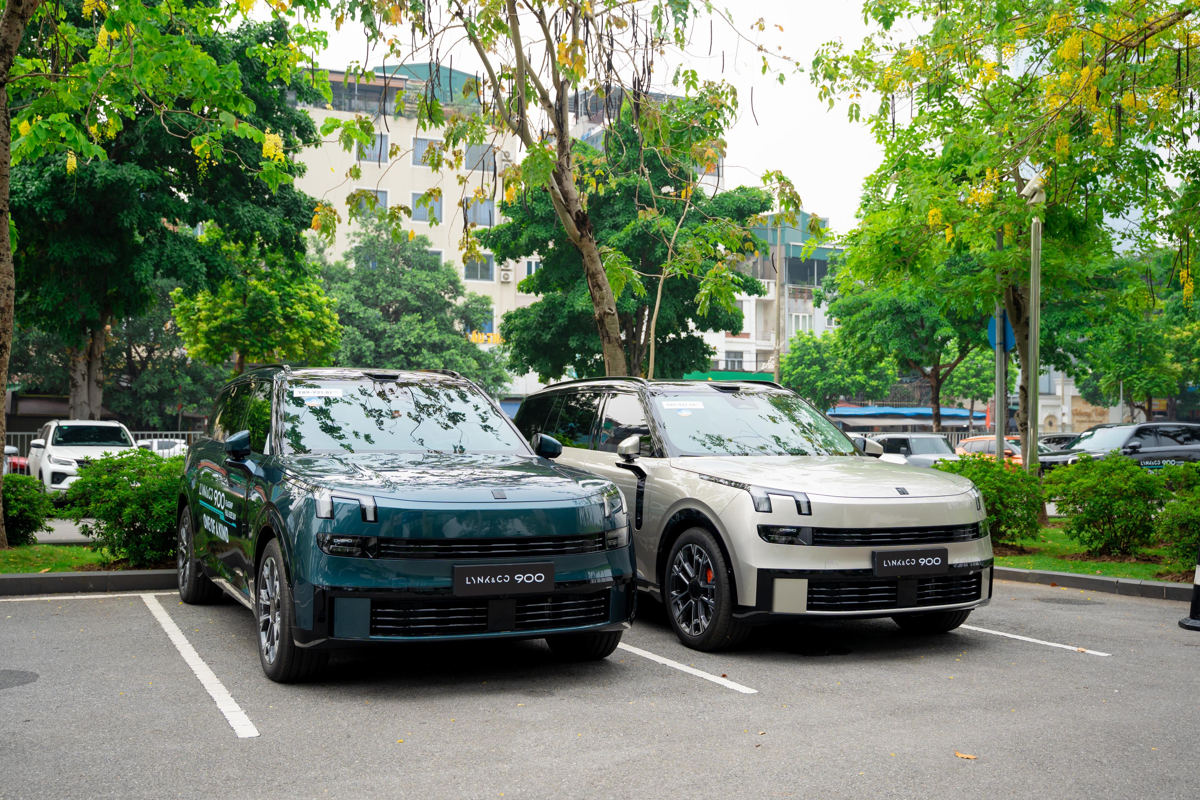 Hai xe Lynk & Co 900 đỗ song song ngoài trời: một xanh đậm, một bạc, góc ba phần tư phía trước.